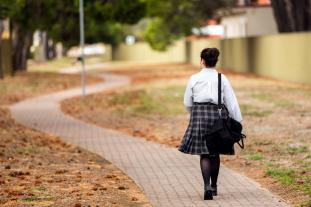 School student walking away from camera down winding Autumnal path